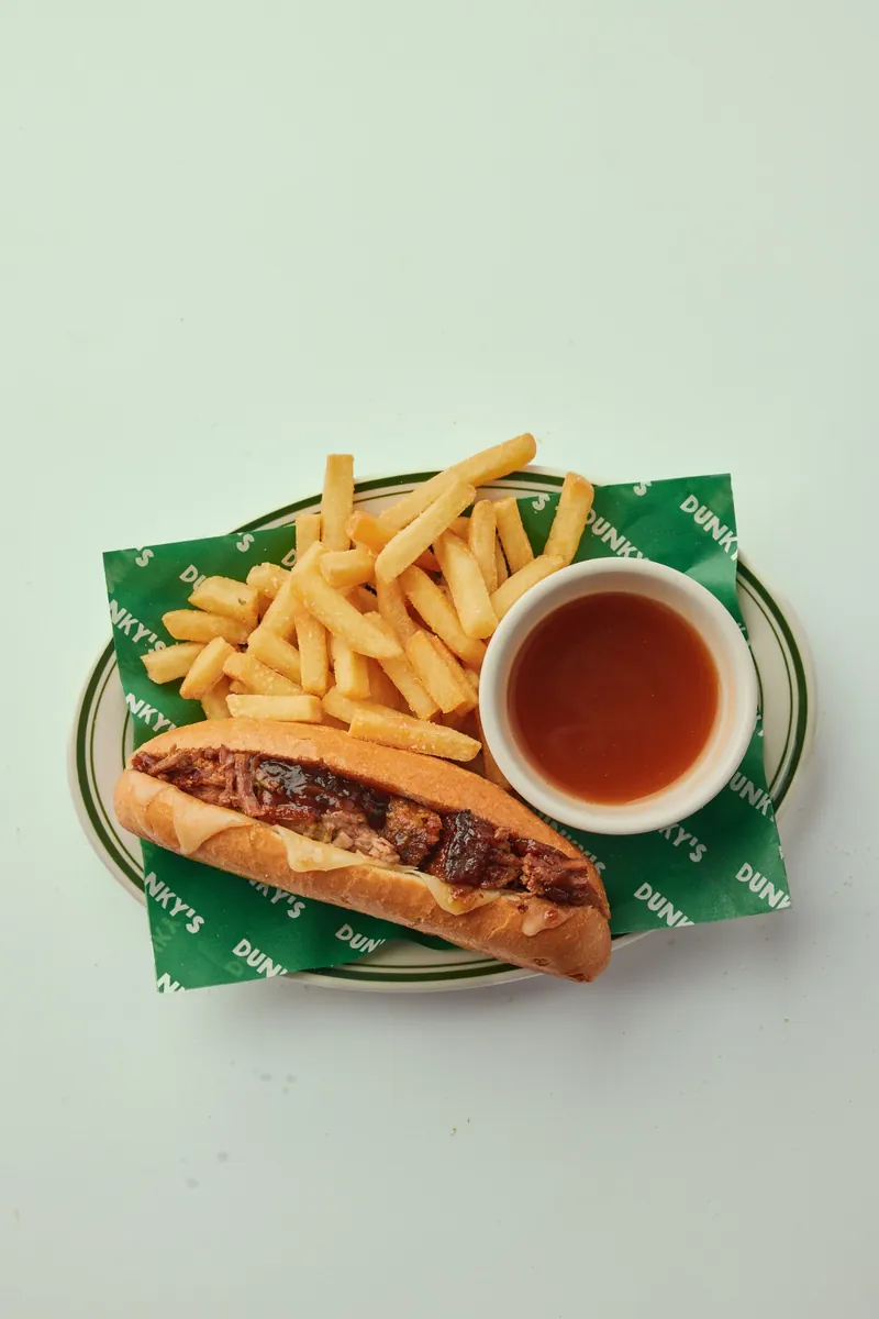 A Dunky's brisket roll with chips and a cup of jus on a Dunky's paper-lined plate
